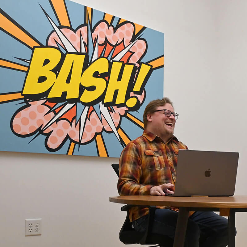 Partner (Tyler) laughing in front of a comic poster